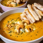 Kürbissuppe mit Schrimps und Brotspieß auf einem Teller.