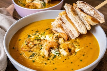 Kürbissuppe mit Schrimps und Brotspieß auf einem Teller.