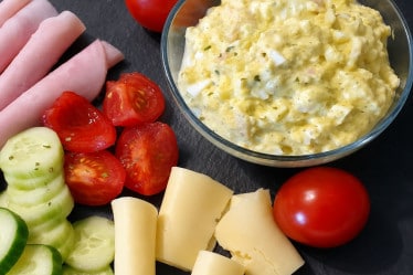 Eiersalat selbstgemacht, angerichtet mit Schinken, Käse, Tomaten und Gurken