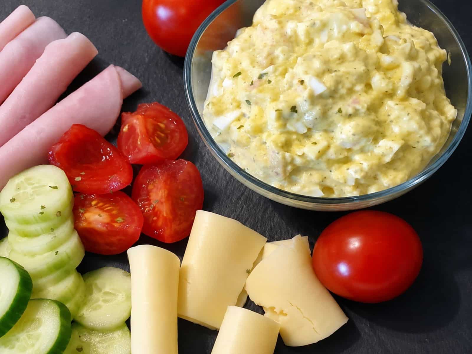 Eiersalat selbstgemacht, angerichtet mit Schinken, Käse, Tomaten und Gurken