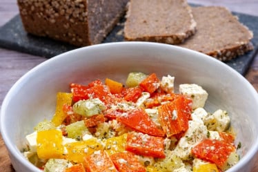 Paprika- Feta- Salat in einer Schüssel mit frischem Brot im Hintergrund