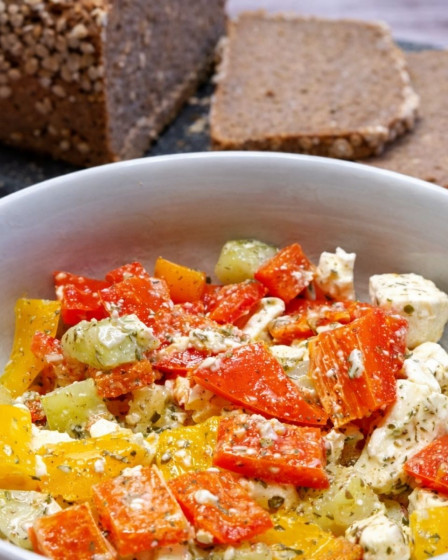 Paprika- Feta- Salat in einer Schüssel mit frischem Brot im Hintergrund