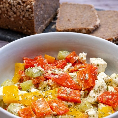 Paprika- Feta- Salat in einer Schüssel mit frischem Brot im Hintergrund