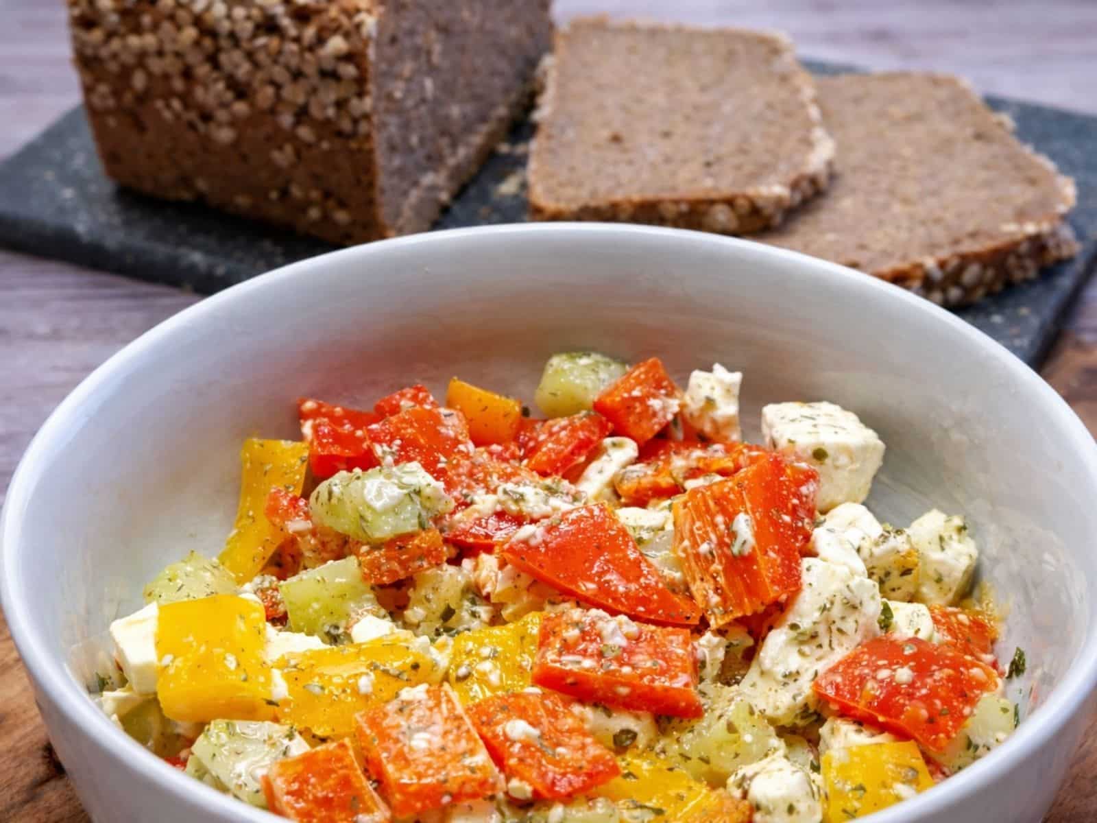 Paprika- Feta- Salat in einer Schüssel mit frischem Brot im Hintergrund