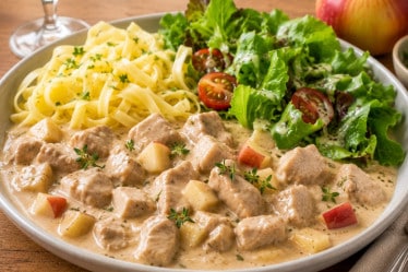 Geschnetzeltes mit Apfel in Weinsoße, Nudeln, Salat auf einem Teller