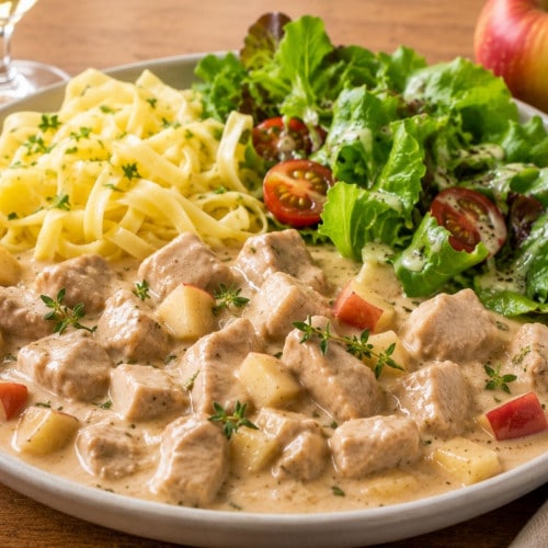 Geschnetzeltes mit Apfel in Weinsoße, Nudeln, Salat auf einem Teller