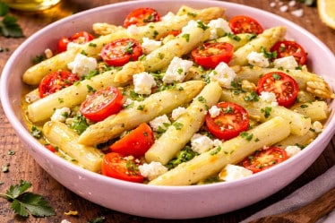 Frischer Spargelsalat mit weißem Spargel, halbierten Cocktailtomaten und Feta in einer rosa Schale