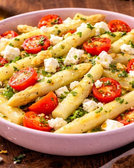 Frischer Spargelsalat mit weißem Spargel, halbierten Cocktailtomaten und Feta in einer rosa Schale