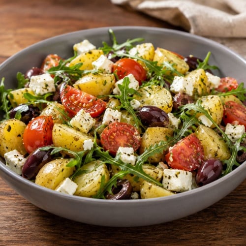 Mediterraner Kartoffelsalat ,it Tomate, Rucola, Feta und Zwiebeln in einer Schüssel auf einem Holztisch