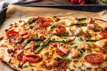 Spargelflammkuchen mit Lachs und Tomaten auf einem Ofenblech