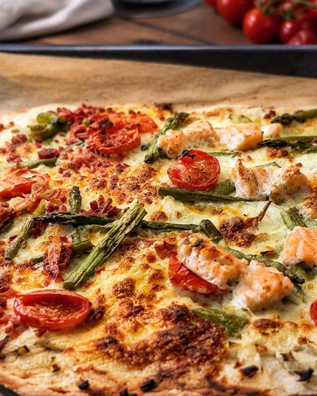 Spargelflammkuchen mit Lachs und Tomaten auf einem Ofenblech