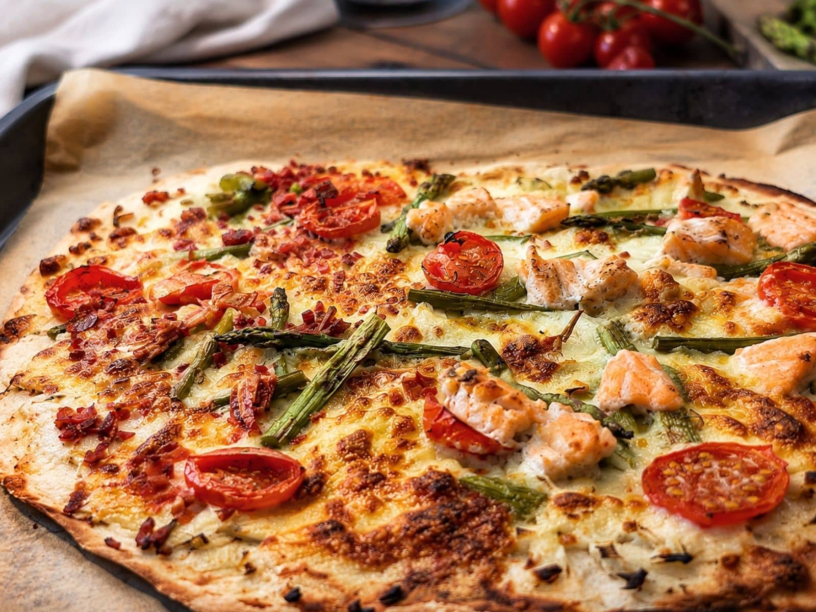 Spargelflammkuchen mit Lachs und Tomaten auf einem Ofenblech