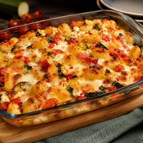 Gnocchiauflauf mit Zucchini, Paprika und Feta in einer Auflaufform auf einem Brett